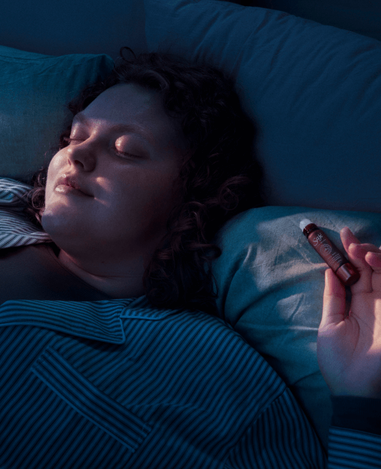 A woman lays sleeping in bed holding a Saje roll-on.