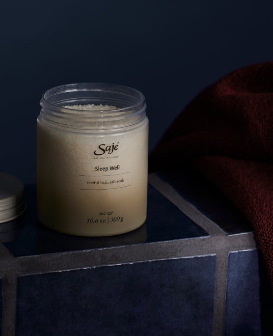 An open jar of white bath salts sits atop a blue-tiled surface against a dark backdrop.