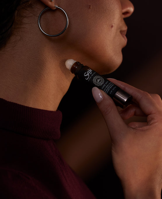 Close-up of a person’s jawline rolling Sleep Well Roll-On on their neck in dim lighting.