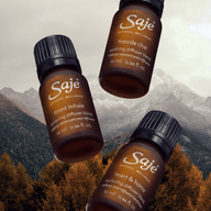 Three brown Saje diffuser blend bottles floating against a mountain backdrop