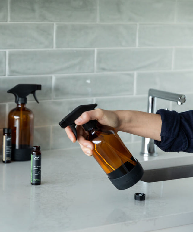 A person spraying a bottle of Saje multi-surface cleaner on a counter