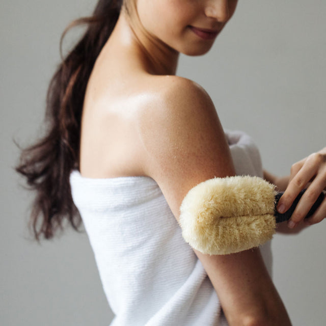 A person in a towel with a ponytail, dry brushing their arm 