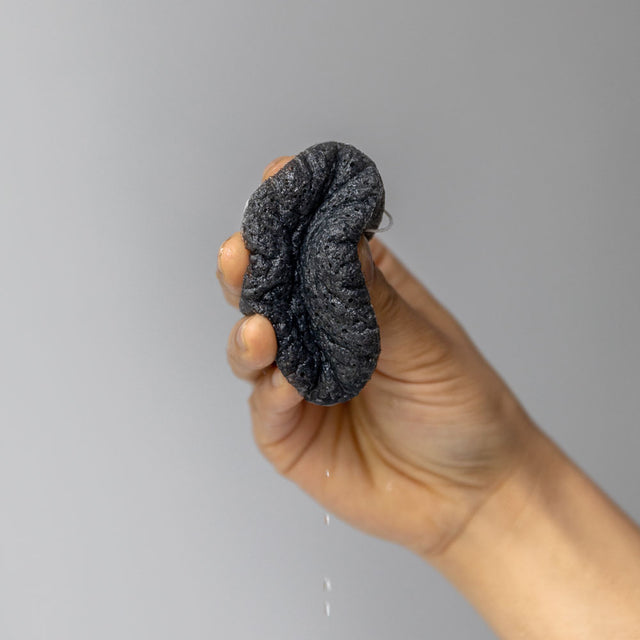 a hand squeezing the Bamboo charcoal purifying vegetable fibre sponge showing water droplets coming out of it